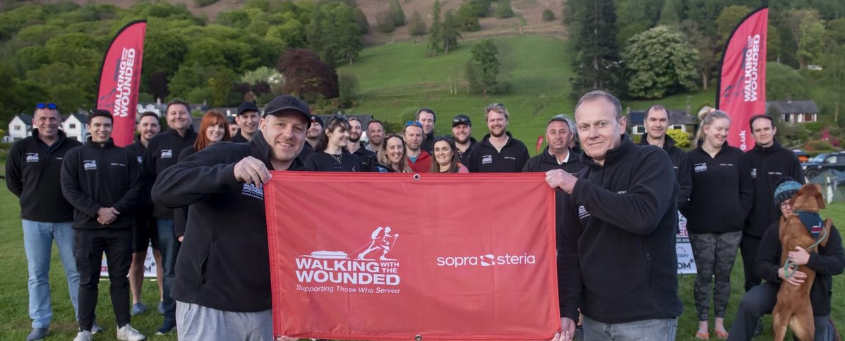 Large group of people in Walking With the Wounded tshirts with two people at the front holding a Sopra Steria Walking With the Wounded flag